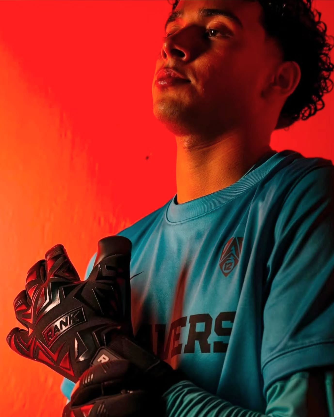 Oregon State Mens soccer goalkeeper, James Romero, wearing a light blue jersey and holding black and red Nike gloves, set against a dramatic red-orange studio background.